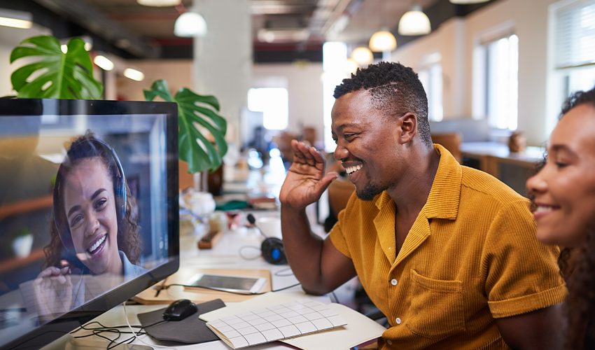 A man waves to his colleague on a video call from his office